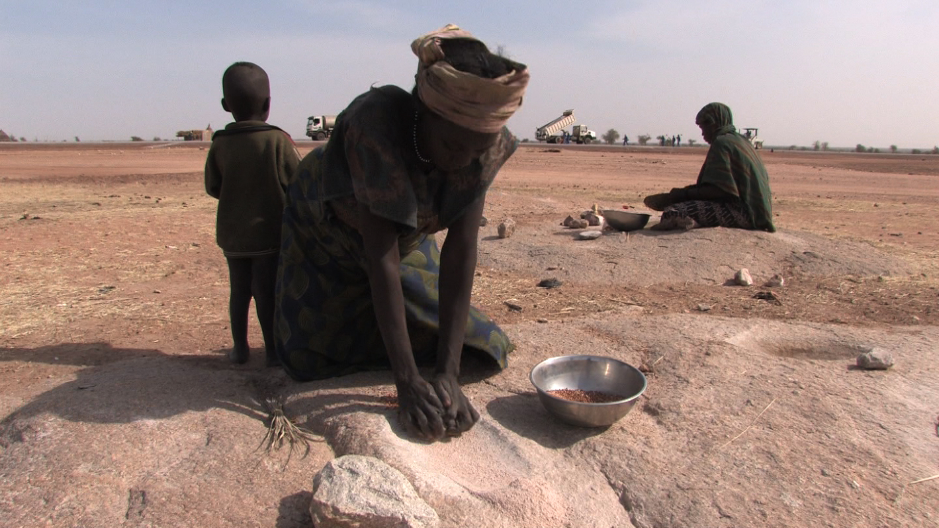Habiter/construire_Kadidja cuisinant, les buildosers en arrière-plan